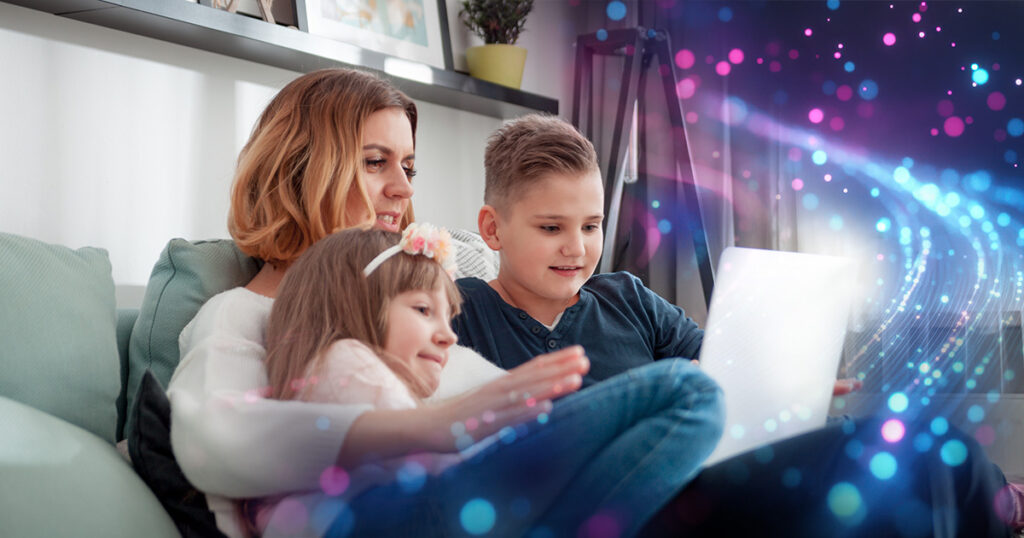 Image of a mother with two young children, sitting on a couch and  ooking at a laptop.