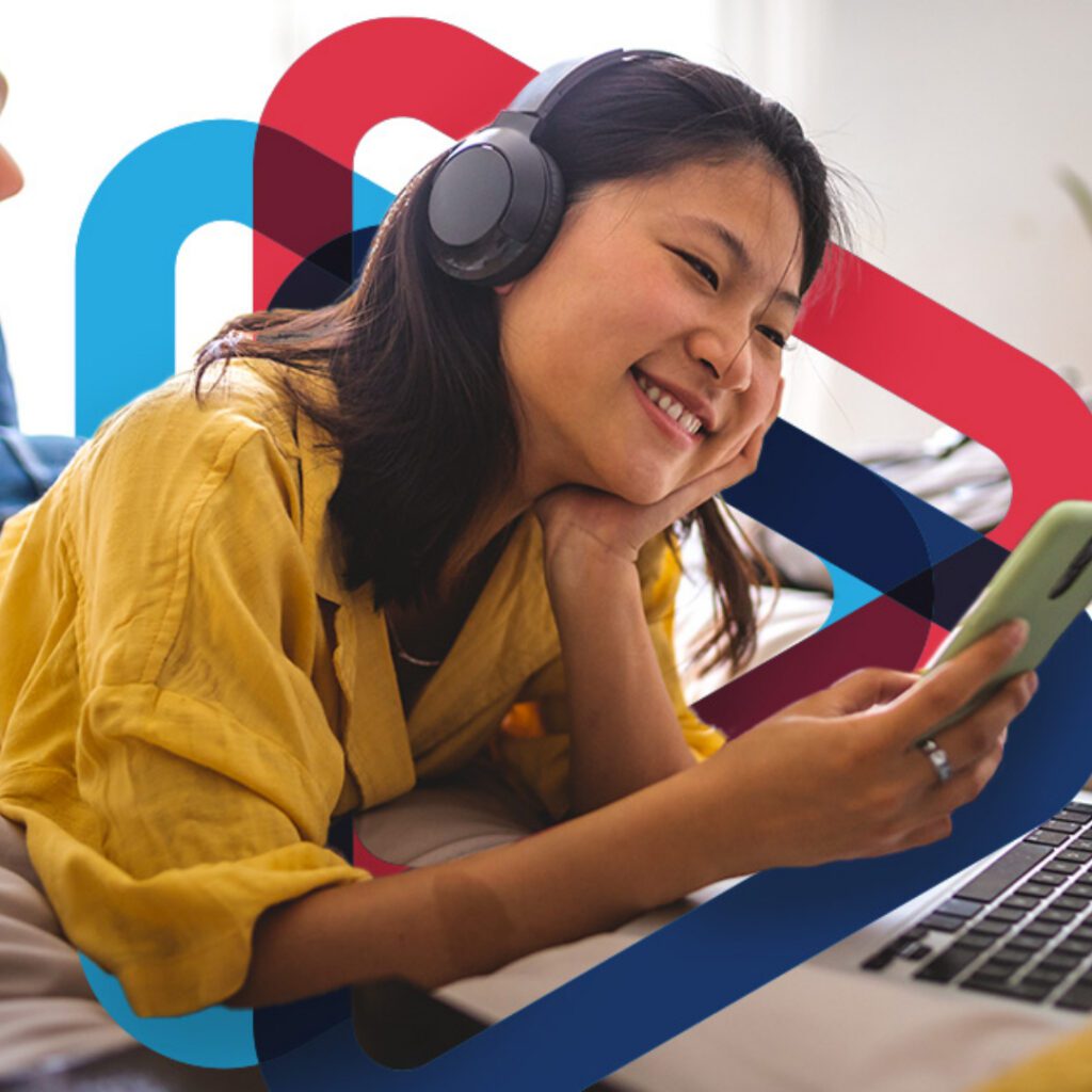 Girl enjoying wireless headphone music and looking at phone infront of computer