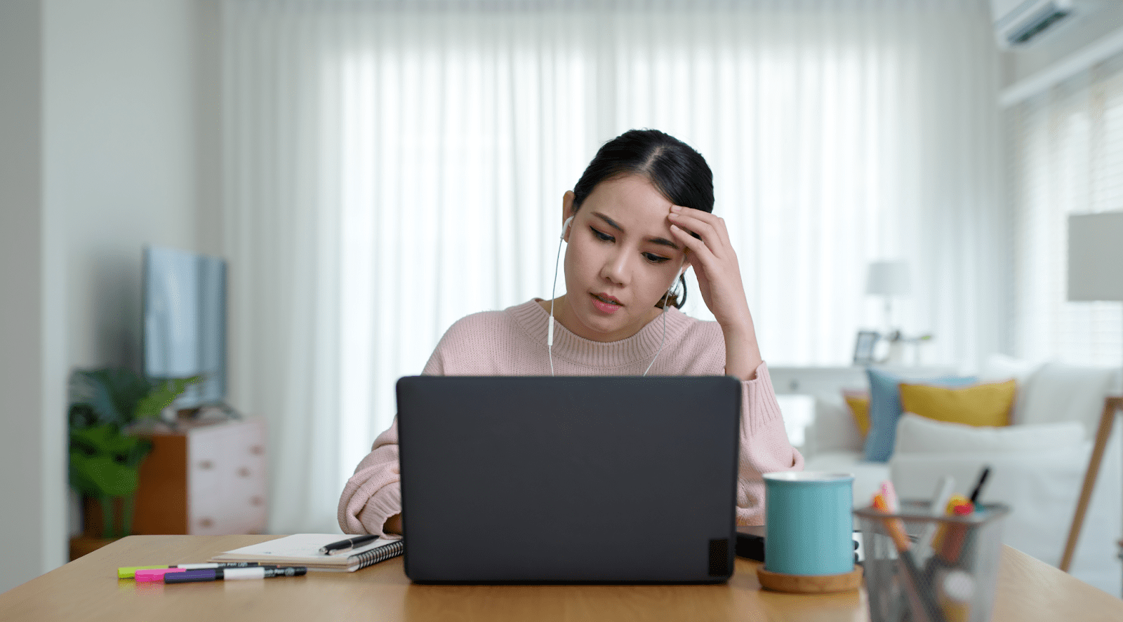 Picture of a young woman wearing in-ear headphones and looking at a laptop.