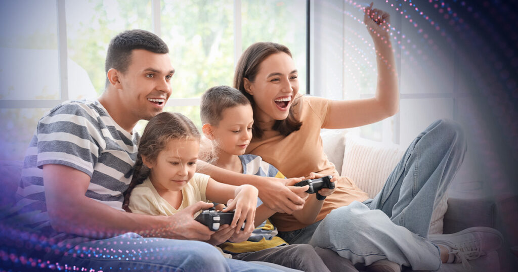 A mother, father, and two young children looking excited while they play a video game together.