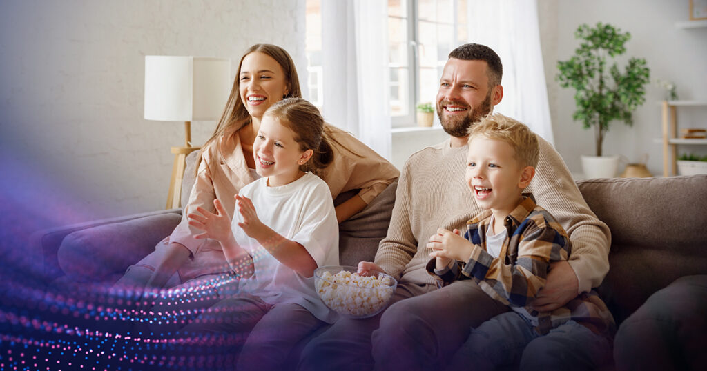 Young family sitting on a couch in their living room eating popcorn and streaming a movie.