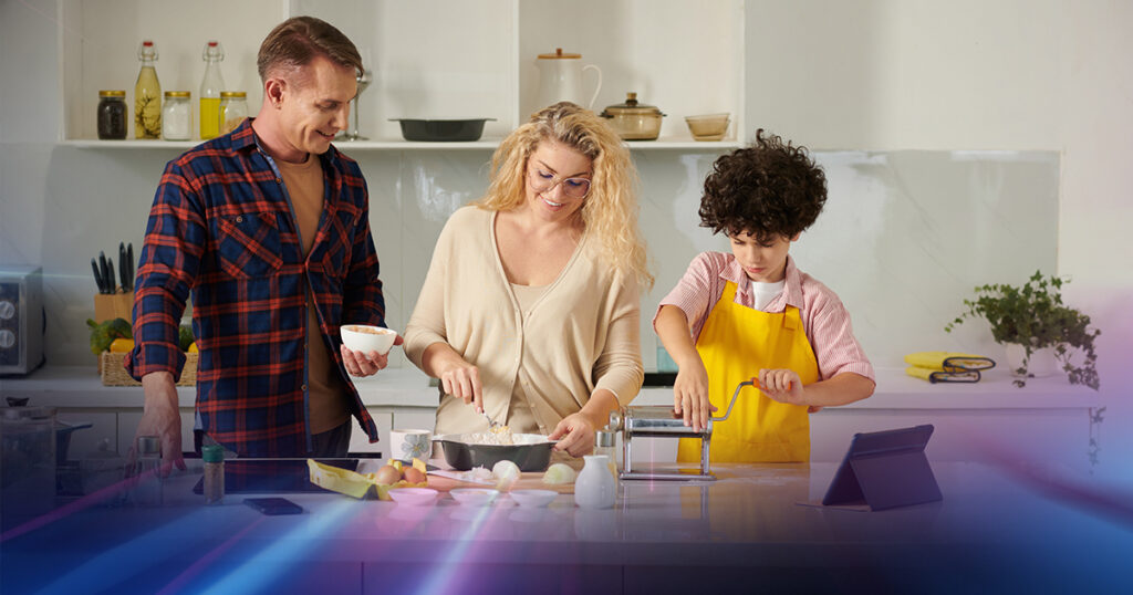 Father, mother, and young son, following a recipe on a tablet while they prepare a meal in the kitchen.