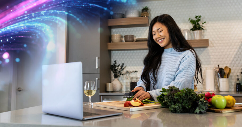 A woman preparing a meal in her kitchen in while using Zoom to connect with someone far away.