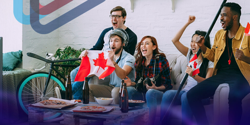 A group of young men and women sitting on a couch and holding canadian flags and cheering.