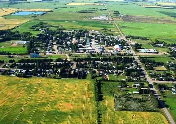 Aerial view of Andrew, Alberta, showing the village's tree lined streets and houses, the main road through town and a ball diamond, with green and yellow farm fields all around