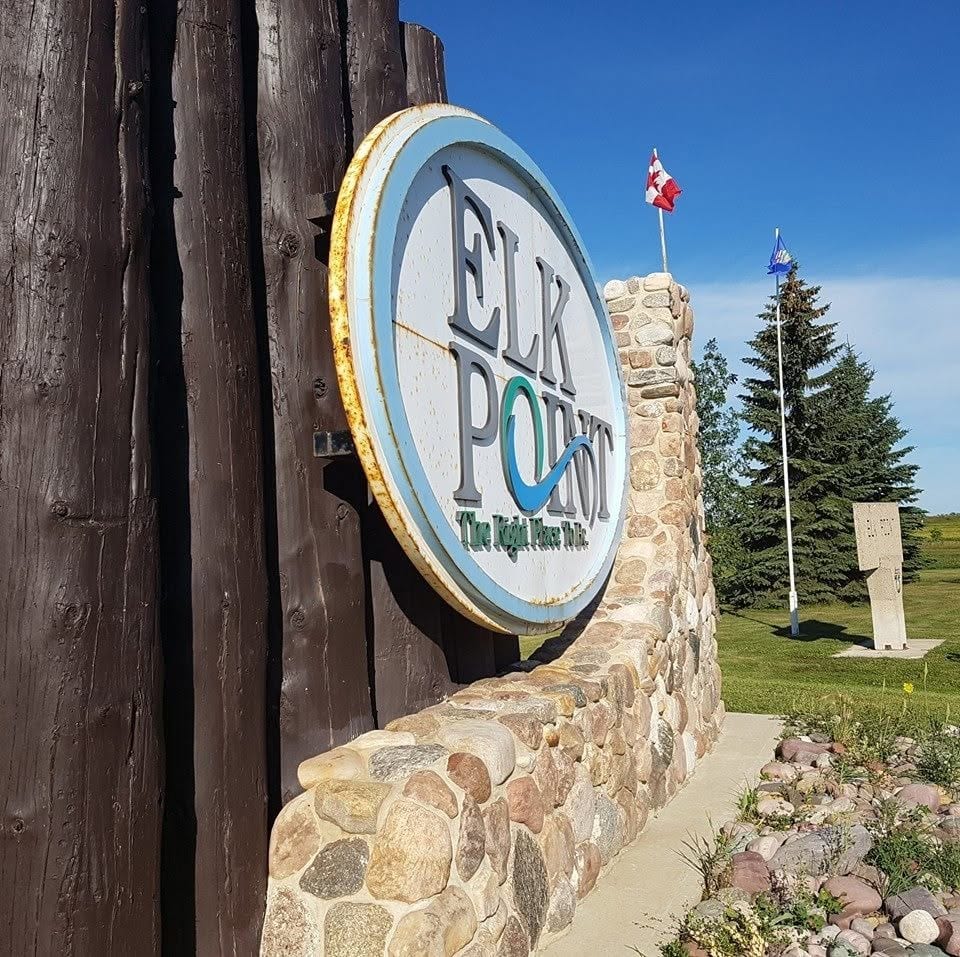The Elk Point town sign in Elk Point, Alberta, a round sign mounted on a timber and fieldstone base with Canadian and Alberta flags flying behind it