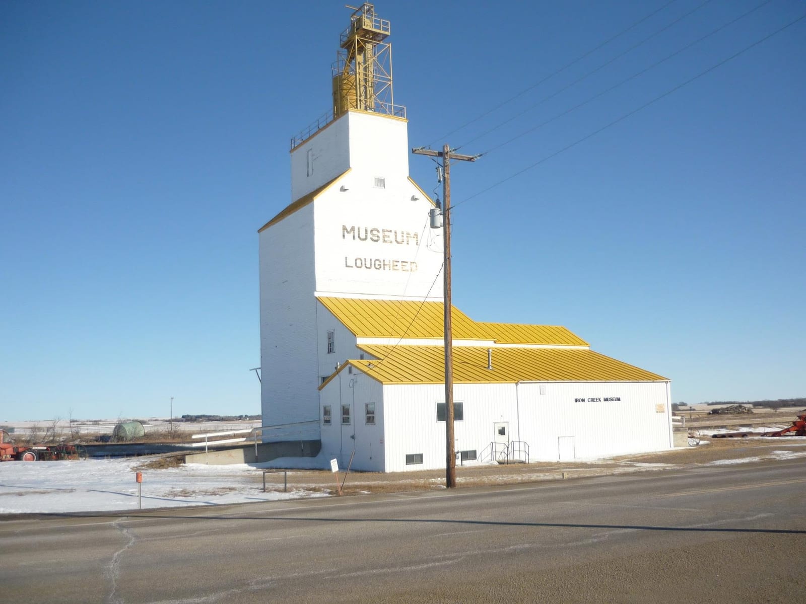 The white and yellow former grain elevator in Lougheed, Alberta, painted with the word Museum, with the Iron Creek Museum building attached alongside and snow on the ground