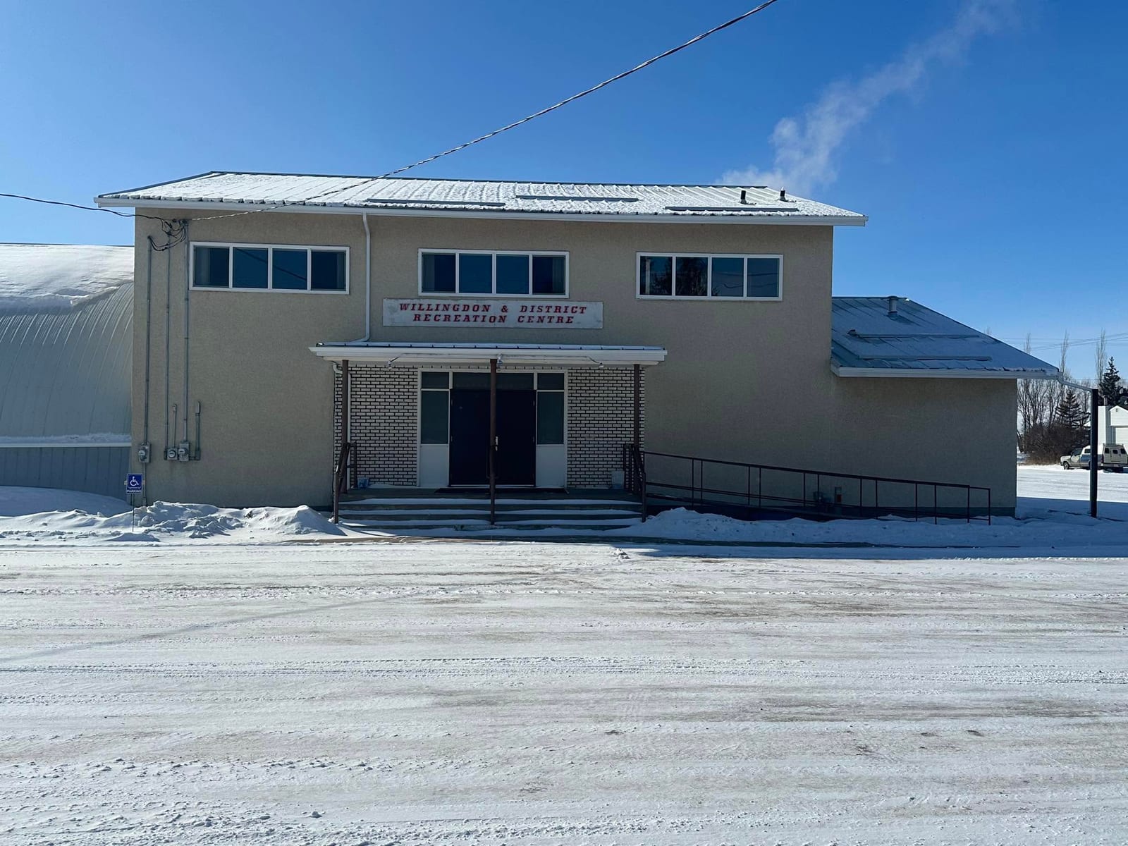 The two-storey Willingdon and District Recreation Centre in winter, its name in red lettering above the entrance, with an arched-roof arena building adjoining it on the left